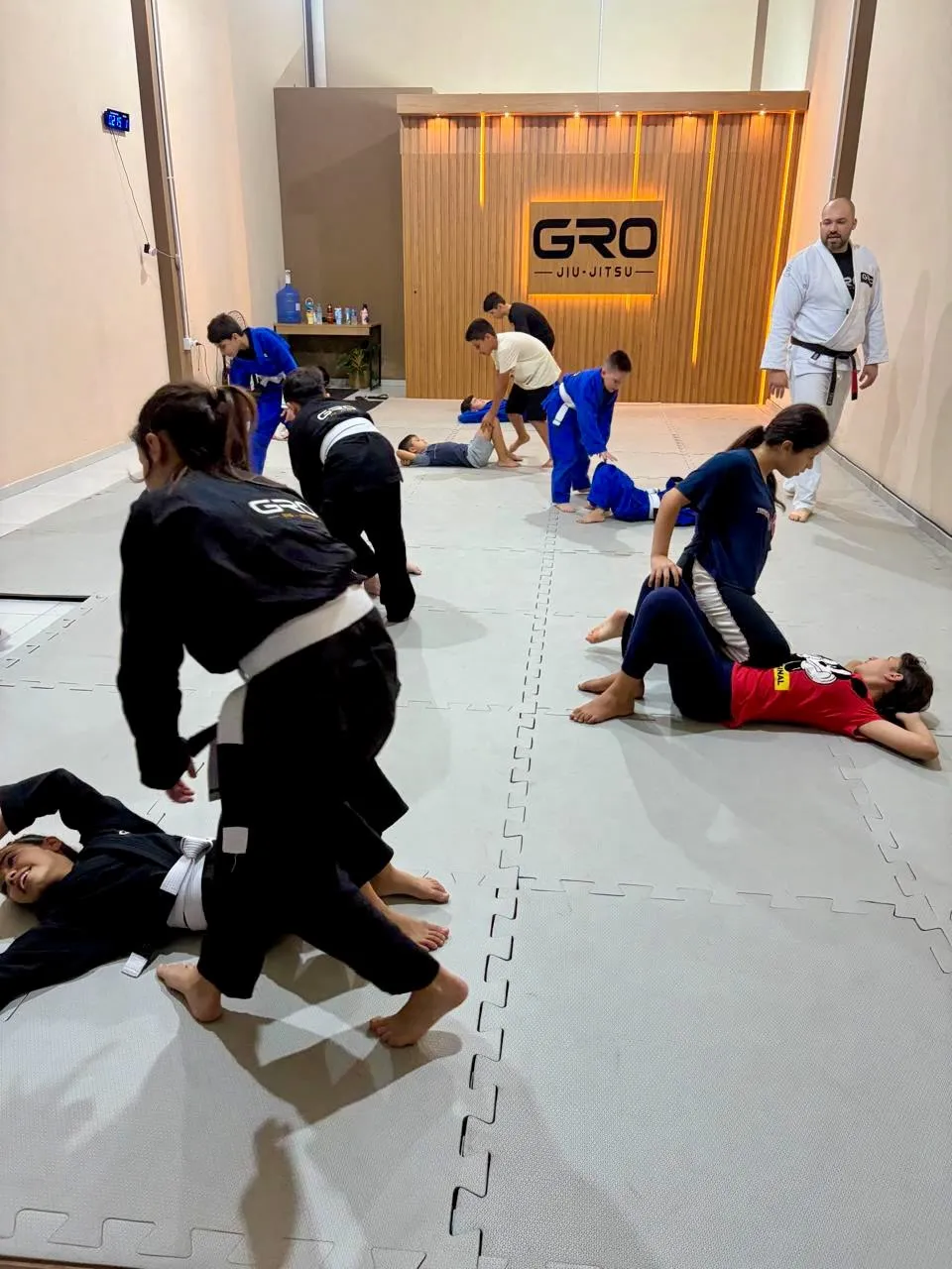 Crianças e adolescentes treinando Jiu-Jitsu em dupla com o professor acompanhando