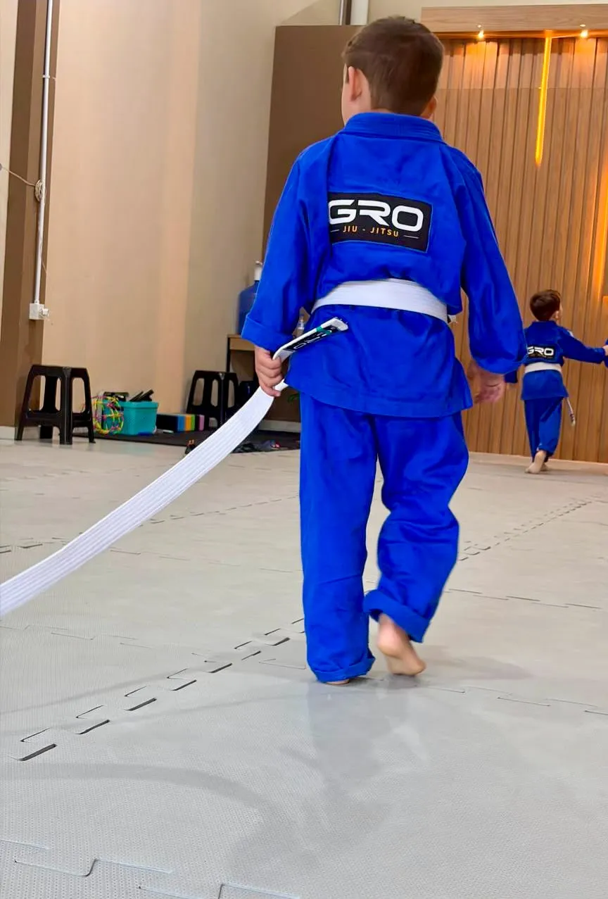Aluno da turma kids da GRO Jiu-Jitsu carregando a faixa branca no tatame